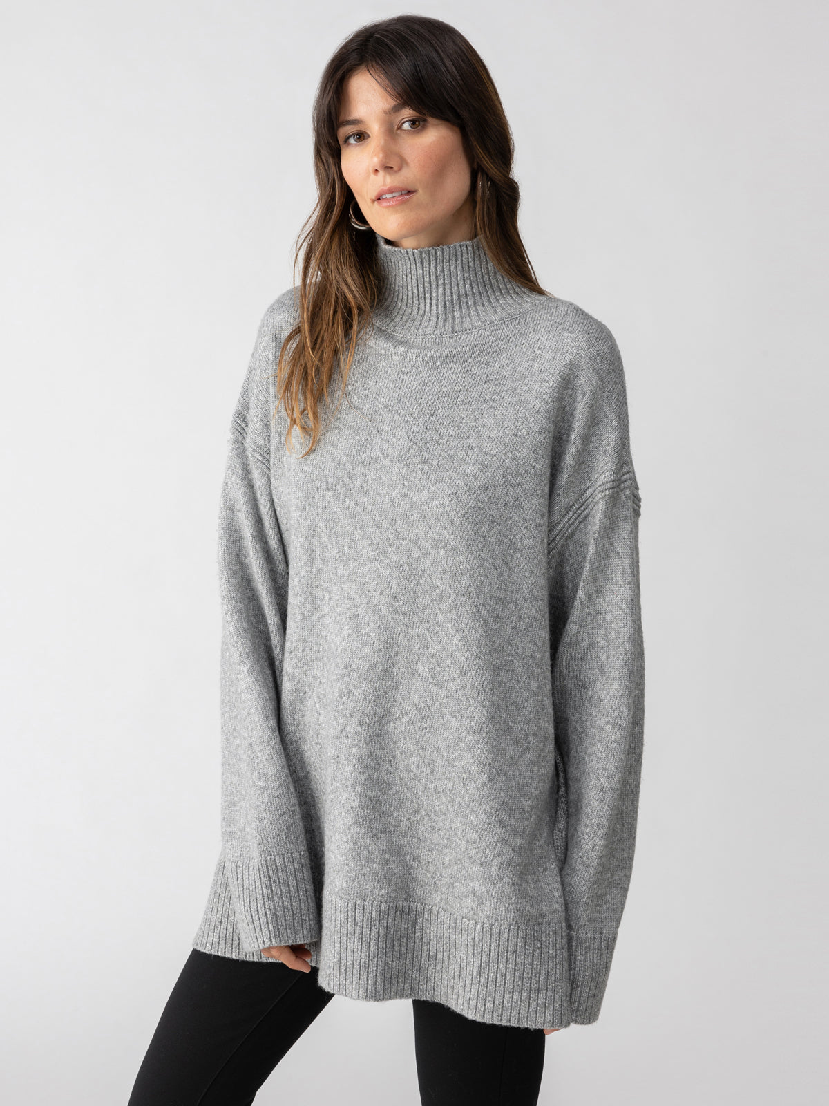 A person is wearing the Perfect Tunic Heather Ash from Sanctuary Clothing, posing against a plain white background. The tunic features an oversized fit with ribbed cuffs and hem. With long dark hair, the individual is looking directly at the camera.