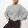 A person poses against a plain background, wearing the Fuzzy Volume Sleeve Sweater in Heather Grey from Sanctuary Clothing and dark cargo pants. Their hair is pulled back, and they look confidently at the camera.