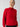 A person wearing the Cable Mock Neck Sweater in Mars Red by Sanctuary Clothing stands against a plain background. They have blond hair pulled back and are gazing off to the side. The sweater boasts a textured pattern along with ribbed cuffs and hem.