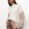 A person with long hair is wearing Sanctuary Clothing's boucle sleeve sweater in light heather oatmeal multi, paired with silky beige pants, and standing against a plain white background.