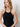 A woman with wavy blonde hair models the Sanctuary Clothing promenade halter dress in black, standing against a plain white background and looking slightly to her left with a neutral expression.