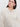 A person with long dark hair is wearing the Sanctuary Clothing open knit bomber jacket in chalk, featuring extended sizing and a zipper. They accessorize with gold hoop earrings and maintain a neutral expression against a plain white background.
