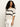 A woman with curly hair wears Sanctuary Clothing's "openwork tee black chalk stripe" over a white top, paired with light-colored pants. She stands against a plain background, looking to her left with one hand in her pocket.