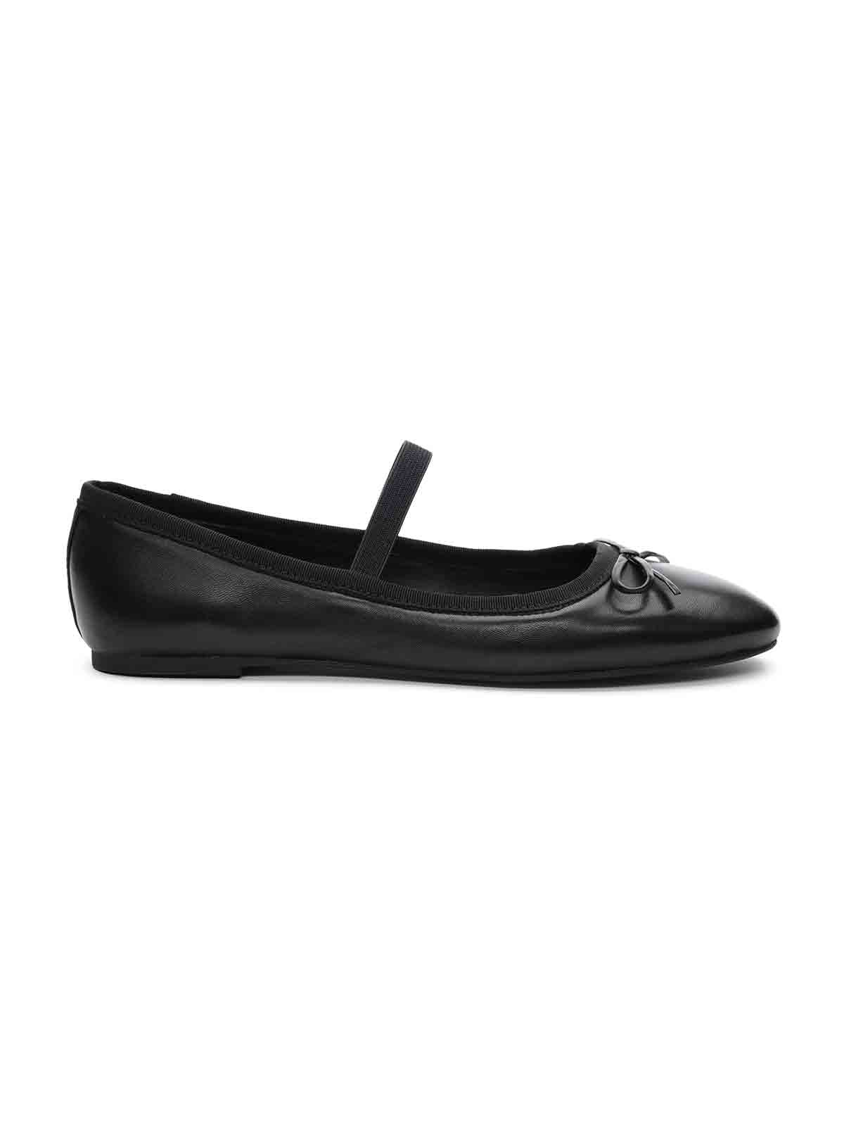 A side view of the Facile Ballet Flat Black by Sanctuary Clothing showcases a sleek black ballet flat adorned with a small bow on the front and an elastic strap along the instep. The shoe boasts a smooth, shiny finish and features a thin sole.