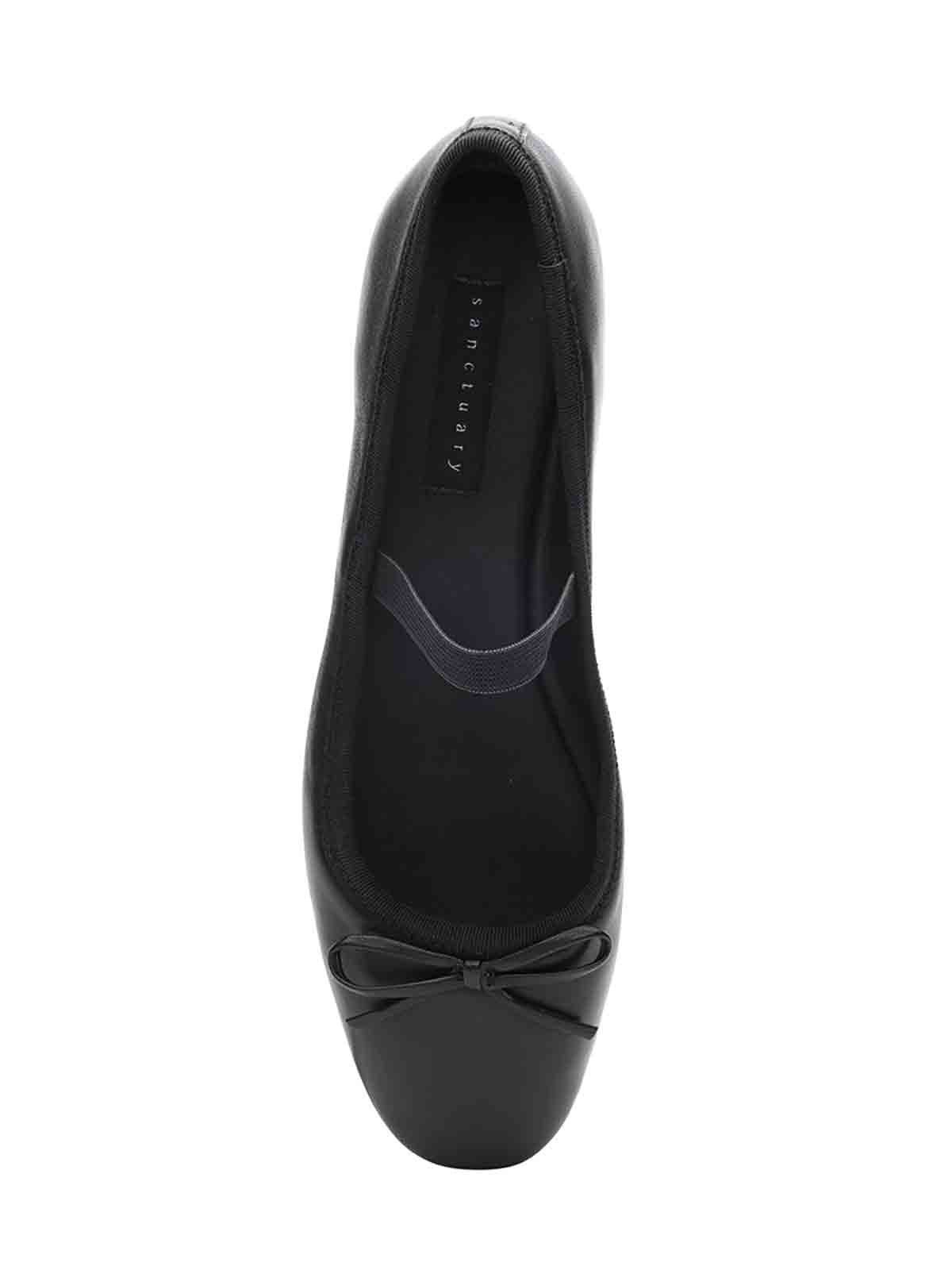 Top view of the Facile Ballet Flat in black with a small decorative bow on the toe area and the brand name "Sanctuary Clothing" visible on the insole. The shoe has a rounded toe and a sleek, minimalist design.