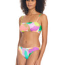 A woman with curly hair is wearing the Daytripper Bandeau Bikini Top Multi from Sanctuary Clothing, featuring a colorful, abstract pattern. She pairs it with matching bikini bottoms and stands while looking slightly off to the side, maintaining a neutral expression against a plain white background.