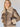 A person with long blonde hair wearing the Zarina Shearling Coat Mink Beige from Sanctuary Clothing, looking at the camera. The coat features a large, fluffy collar and cuffs, with a zipped front. The background is plain and light-colored.