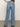 A person is seen from behind wearing Sanctuary Clothing's ekara slim wide jeans light, featuring a high waist and slightly flared leg. They stand on a neutral floor against a light backdrop, one hand in their pocket.