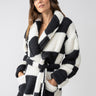 A woman wearing the Shawl Collar Teddy Robe in Black Check by Sanctuary Clothing, featuring a black and white pattern with pockets, stands against a neutral background.