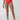 A person is wearing the Sanctuary Clothing refresh rib V-waist high-leg bikini bottom in Mars Red, accompanied by black sandals with white straps. The background is plain and minimalistic, highlighting the swimwear and sandals.